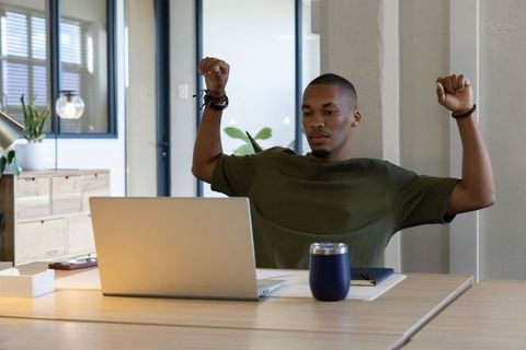 African american man stretching at modern desk with laptop tumbler notebook in daylight