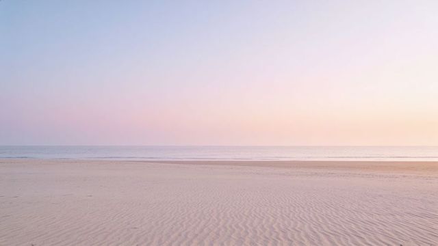 Pastel sunrise over empty rippled beach with calm sea and minimal horizon at dawn