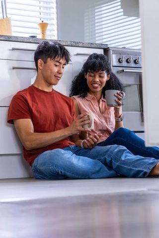 Couple sitting on kitchen floor sipping coffee, smiling morning routine, cozy home moment