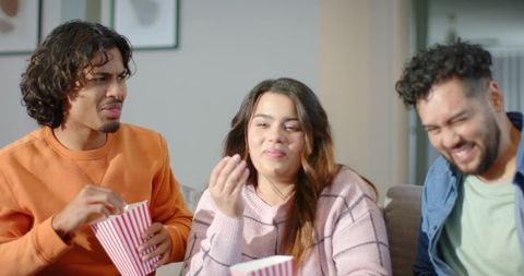 Friends sharing popcorn and reacting during cozy movie night on sofa