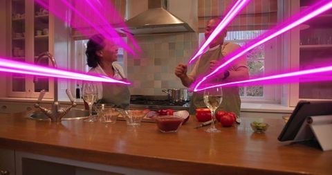 Couple cooking and chopping tomatoes with tablet while playful magenta light beams