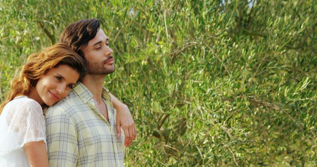 A young Caucasian couple enjoys a romantic moment outdoors, with copy space. Their affectionate embrace amidst the greenery suggests a peaceful and loving relationship.