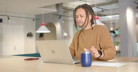 African American man working at laptop in modern coworking space with smartwatch and mug