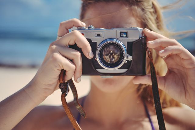 Close-up of woman holding vintage camera on sandy beach. Perfect for travel blogs, vacation advertisements, photography courses, and summer holiday promotions.