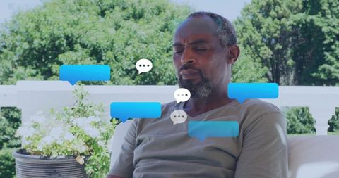 Mature african man relaxing on porch with floating chat bubbles and notifications