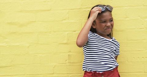 Happy Girl Holding Sunglasses Against Bright Yellow Brick Wall