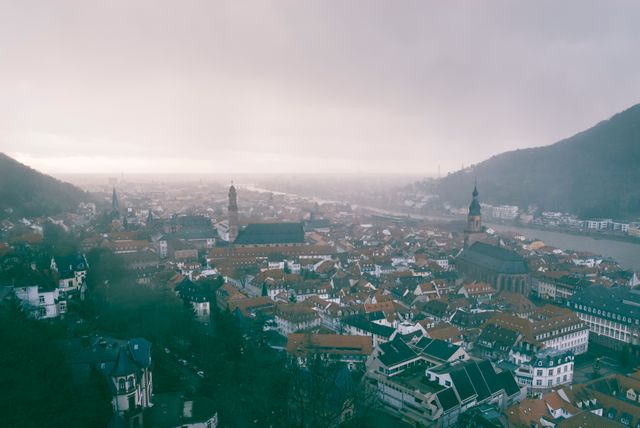 Panoramic view capturing a foggy morning over a historic European city with notable old-town architecture. Features red rooftops, prominent church steeples, and a serene atmosphere ideal for showcasing European travel, historical sites, misty cityscapes, and moody weather settings.