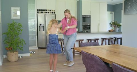Mother and daughter dancing while preparing snack in bright modern family kitchen