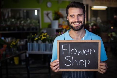 Smiling florist with chalkboard sign in vibrant shop