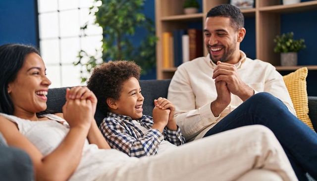 Laughing family clapping and playing game on cozy sunlit living room couch