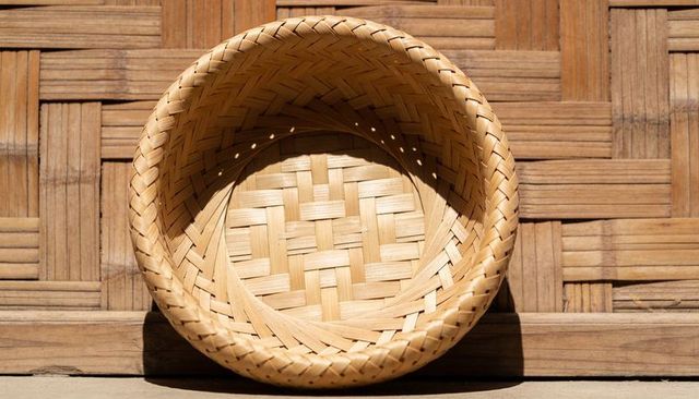 Round woven bamboo basket casting sunlit shadows across rustic woven panel background
