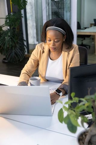 African american woman working on laptop at modern minimalist office desk with greenery