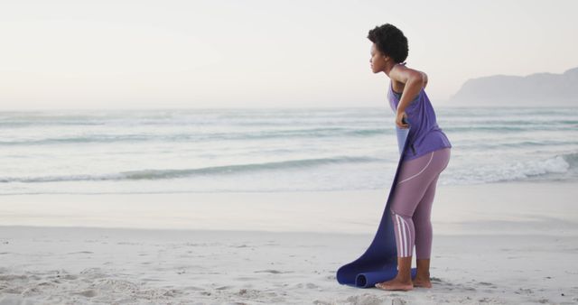 African american woman with yoga mat on sunny beach. healthy and active time beach holiday.