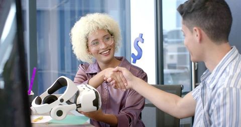 Female tech professional shaking hands with associate over virtual reality headset