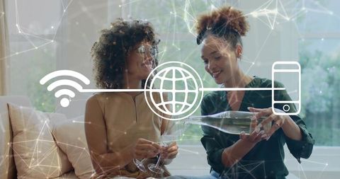 Two friends pouring wine at home with digital wi-fi network overlay for connected living
