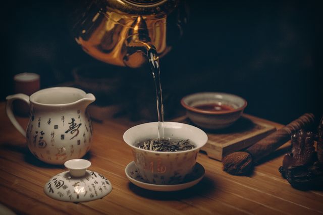 Traditional Chinese tea ceremony scene with tea being poured from authentic teapot into a teacup. This can be used for articles or blogs about Chinese culture, tea rituals, or relaxation techniques. It is suitable for advertisements or promotions for tea products, tea houses, or wellness spas. The scene conveys tranquility and cultural heritage, making it suitable for educational content regarding traditional practices.