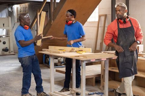 Instructor guiding apprentices passing wood planks in carpentry workshop teamwork training