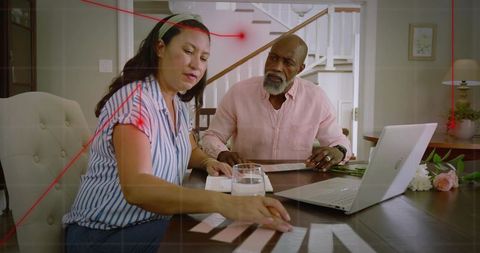 Couple sorting bills and budgeting papers at dining table with laptop and notes