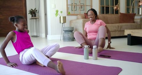 African mother and daughter exercising at home on purple yoga mats, smiling during workout