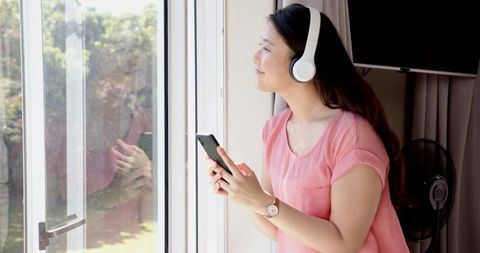 Young Woman Relaxing with Headphones by Sunny Window