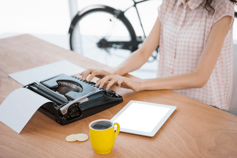 Woman typing on vintage typewriter with digital tablet on transparent desk