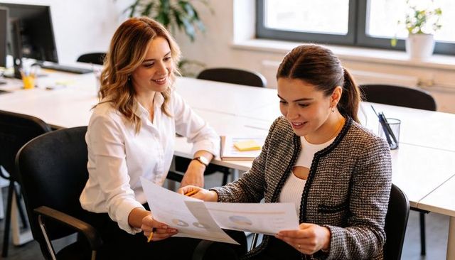 Female colleagues collaborating over printed charts reviewing data and planning office strategy