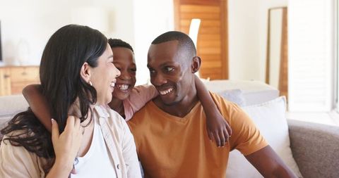Smiling family bonding on sofa, child hugging parents in cozy living room