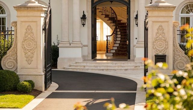 Ornate stone pillars opening to wrought-iron gates revealing grand spiral staircase