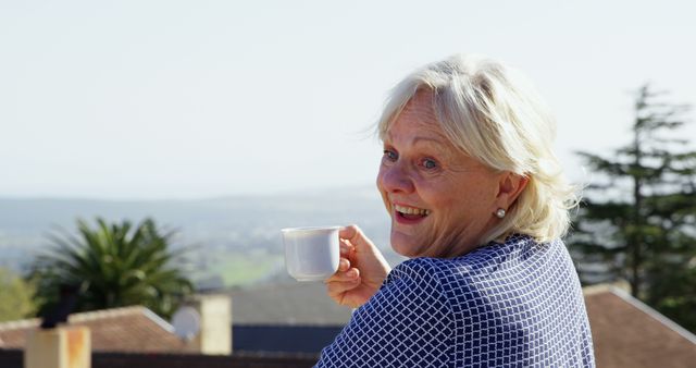 Senior Caucasian woman enjoys a cup of coffee outdoors, with copy space. She exudes a sense of relaxation and contentment with a scenic backdrop.