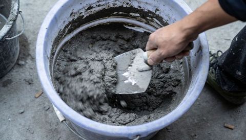Close-up overhead of construction worker stirring cement in blue bucket with metal trowel