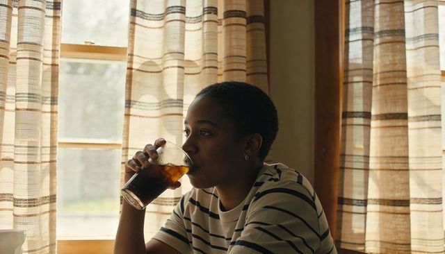 Sipping cold drink by sunlit window, striped shirt, cozy calm morning reflection