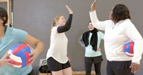 Female volleyball players celebrating high-five during indoor practice, teamwork and energy
