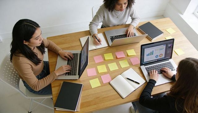 Young women collaborating on laptops, arranging sticky notes and analyzing data charts