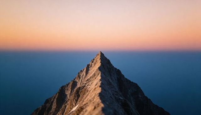 Jagged alpine peak rising into pastel sunset sky with narrow ridgeline and snow patches