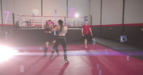 Female fighters sparring while coach approaching raised ring in boxing gym with lens flare