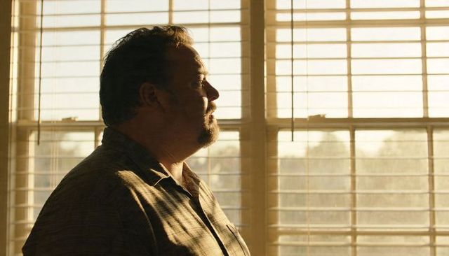 Midlife man standing and looking through window blinds at golden hour, contemplating