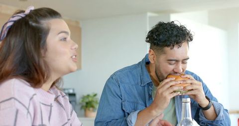 Couple enjoying casual burger lunch in sunlit home kitchen