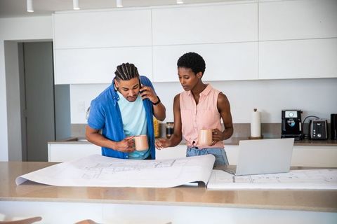 Couple Analyzing Blueprints in Modern Kitchen with Coffee Mugs