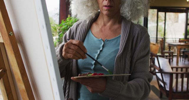 Senior biracial woman painting on balcony. retirement and senior lifestyle, spending time alone at home.