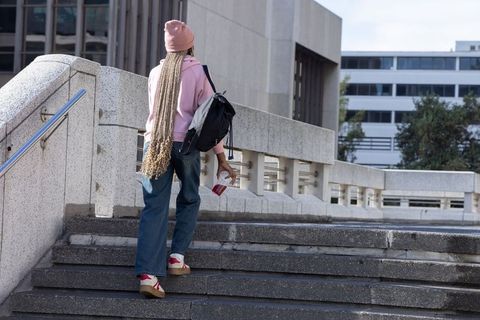 African american woman climbing urban campus stairs wearing pink beanie and backpack