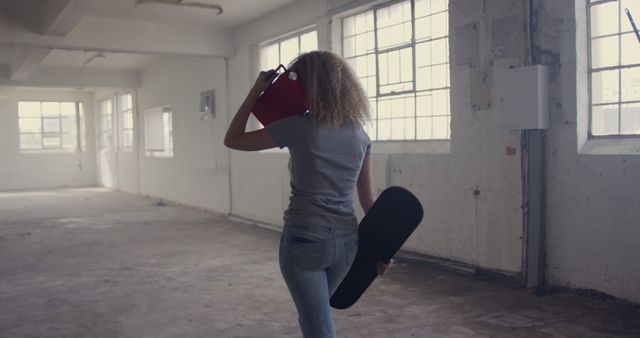 Woman with Afro Hair Carrying Skateboard in Industrial Warehouse - Download Free Stock Images Pikwizard.com