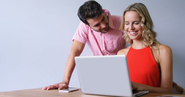 Smiling cute couple using laptop in office