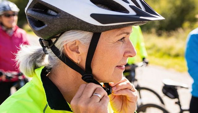 Senior woman fastening bicycle helmet before group ride on sunny park path