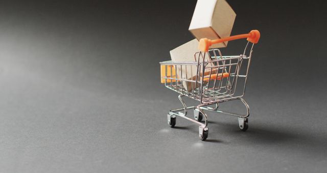 This image depicts a miniature shopping cart containing small boxes, set against a dark background, highlighting themes of e-commerce, retail, and consumerism. Ideal for promotional materials, website banners, blogs about shopping trends, and presentations on modern retail.