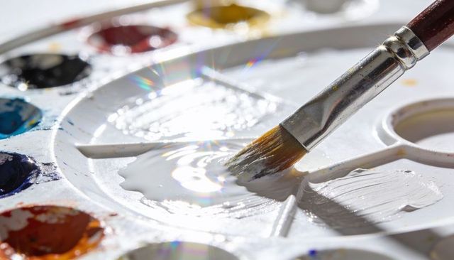 Mixing white paint with brush on plastic palette closeup glossy ripple and iridescence