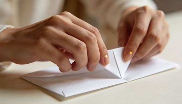 Hands Folding Origami Paper Boat Close-up in Warm Neutral Light
