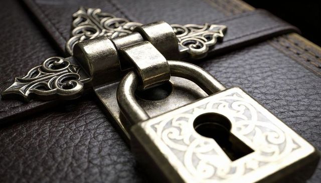 Antique brass padlock securing ornate leather journal with filigree hinge and keyhole