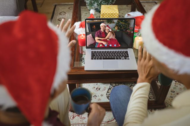Diverse couple with santa hats having video call with happy caucasian couple. Christmas, celebration and digital composite image.