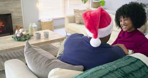 Diverse couple enjoying cozy Christmas evening on sofa with Santa hat and fireplace