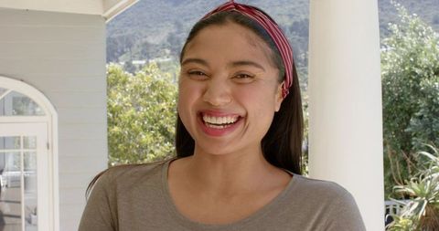 Smiling young woman on sunlit porch wearing red headband and casual gray top